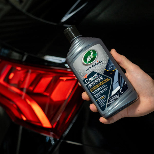 Hand holding Turtle Wax Hybrid Solutions Ceramic Acrylic Black Polish for black car paint. It corrects, enhances, and protects.