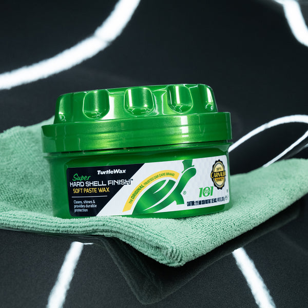 Green Turtle Wax Super Hard Shell Finish Soft Paste Wax sitting on a green cloth on a reflective dark surface.